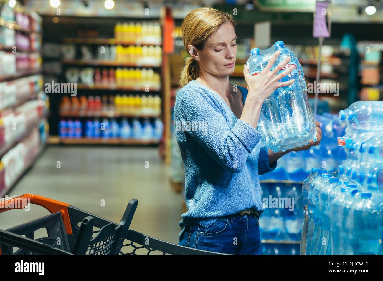 Una donna spaventata e triste in una crisi acquista acqua in un supermercato, immagazzina acqua potabile Foto Stock