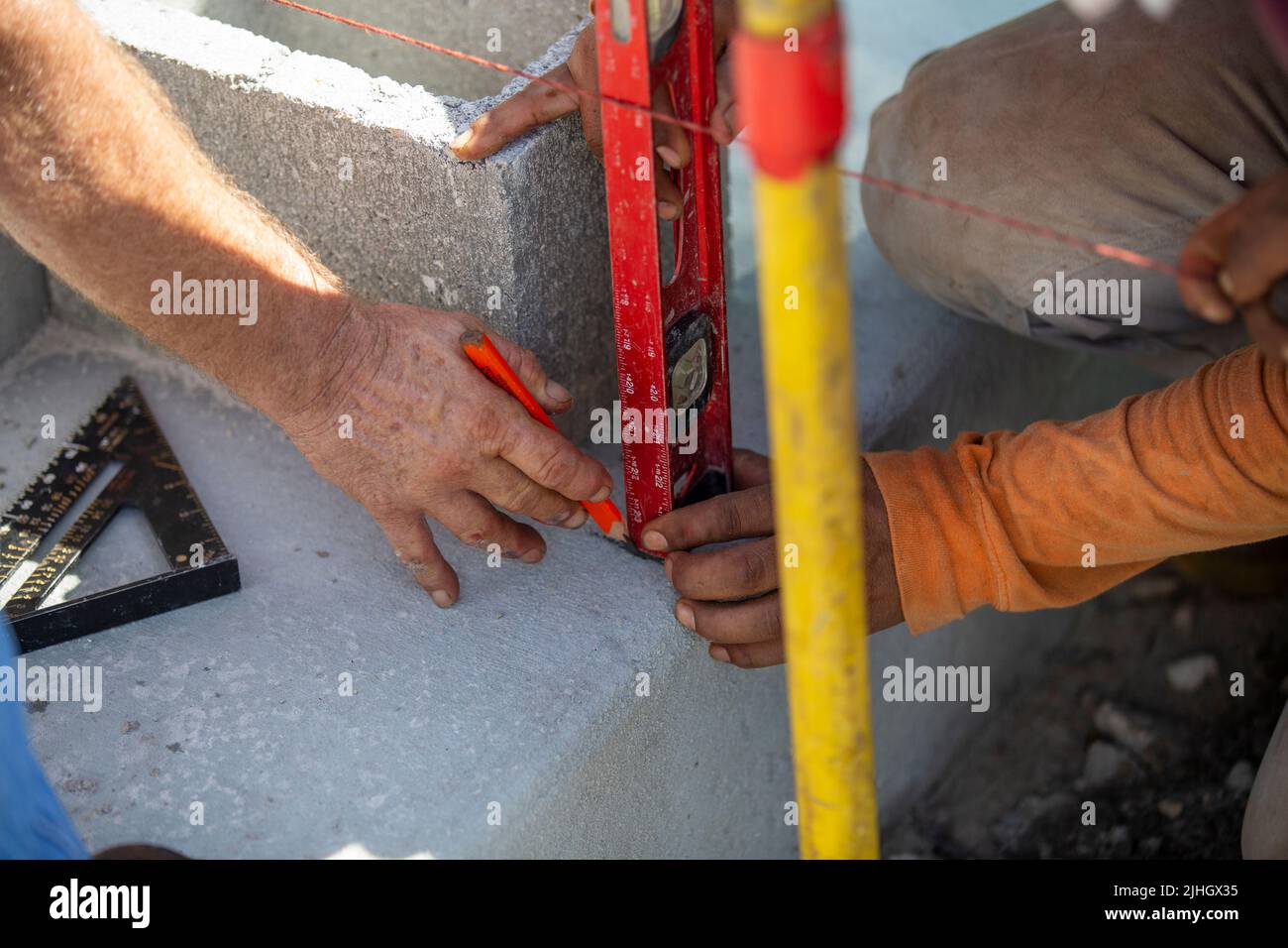 i lavoratori edili tracciano linee su una lastra di calcestruzzo, misurate da un livello e hanno installato una corda in muratura con una matita. Foto Stock