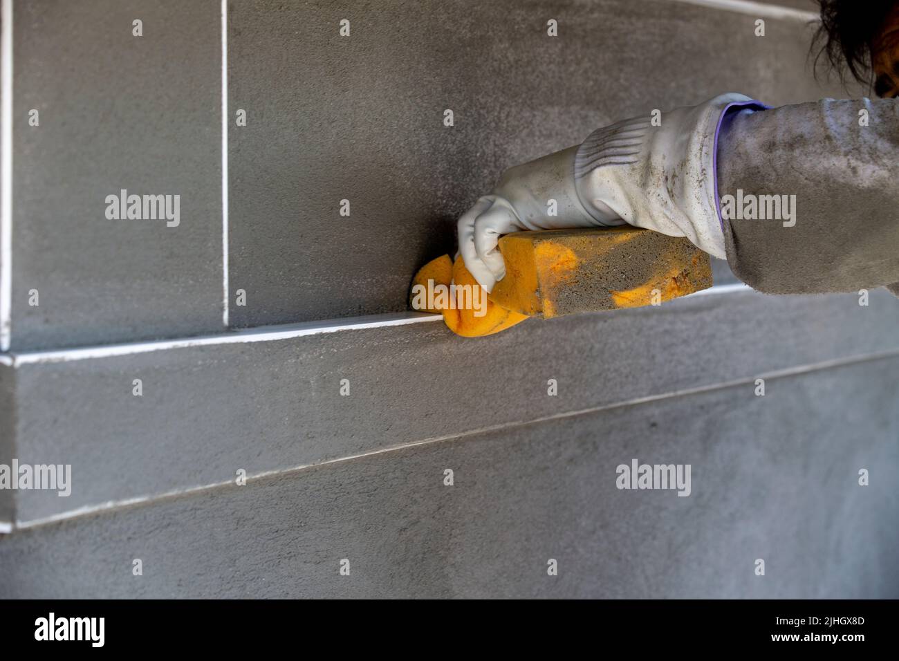 Tecnico di costruzioni esperto che utilizza una spugna bagnata per rimuovere qualsiasi stucco dai bordi della bordatura angolare e levigare lo stucco Foto Stock
