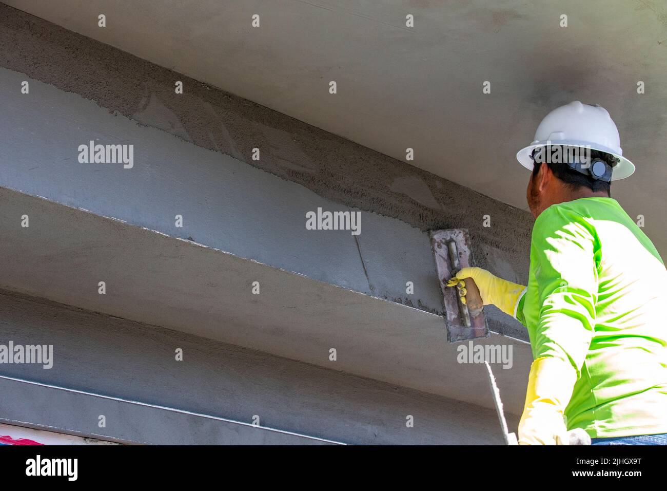 Professionista della costruzione che utilizza una cazzuola per applicare fango di stucco all'esterno di un edificio multiplex, Foto Stock