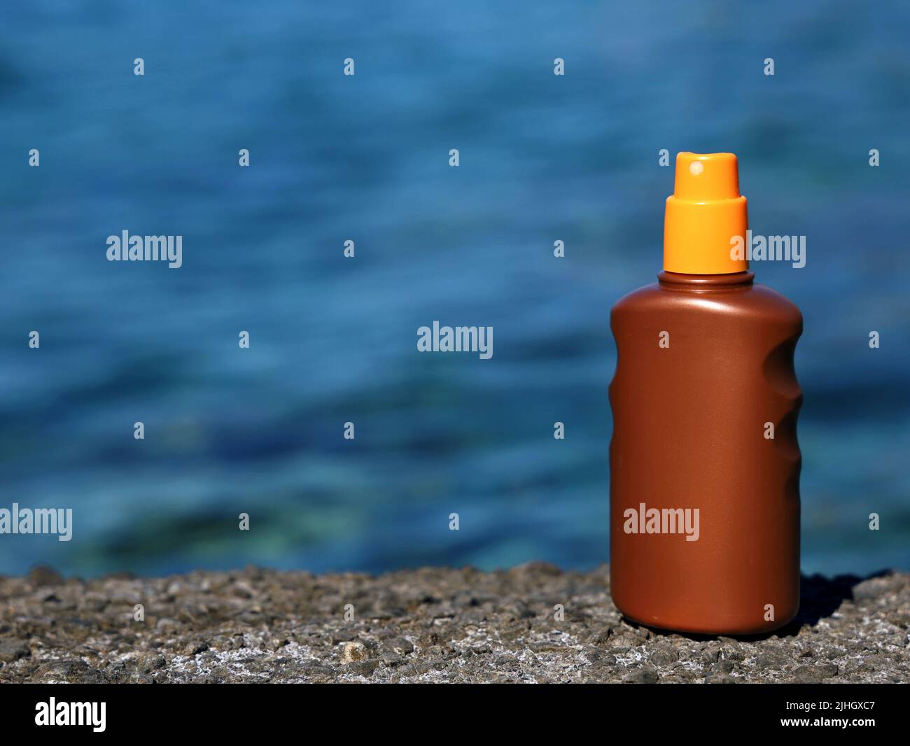 Bottiglia spray crema solare sulla riva di pietra con fondo blu di acqua di mare con spazio per la copia Foto Stock