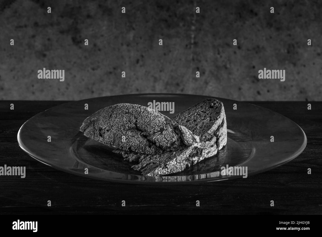 Due pezzetti di pane su una grande lastra di vetro contro un muro sporco ruvido. Foto in bianco e nero scuro Foto Stock