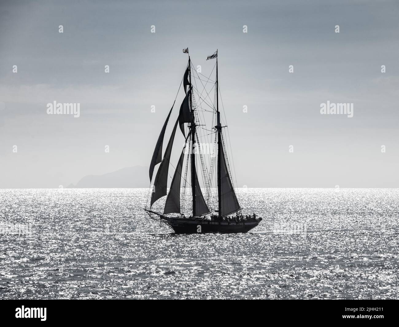 Silhouette di goletta a vela retroilluminata mentre passa San Clemente Island al largo della costa californiana. Foto Stock