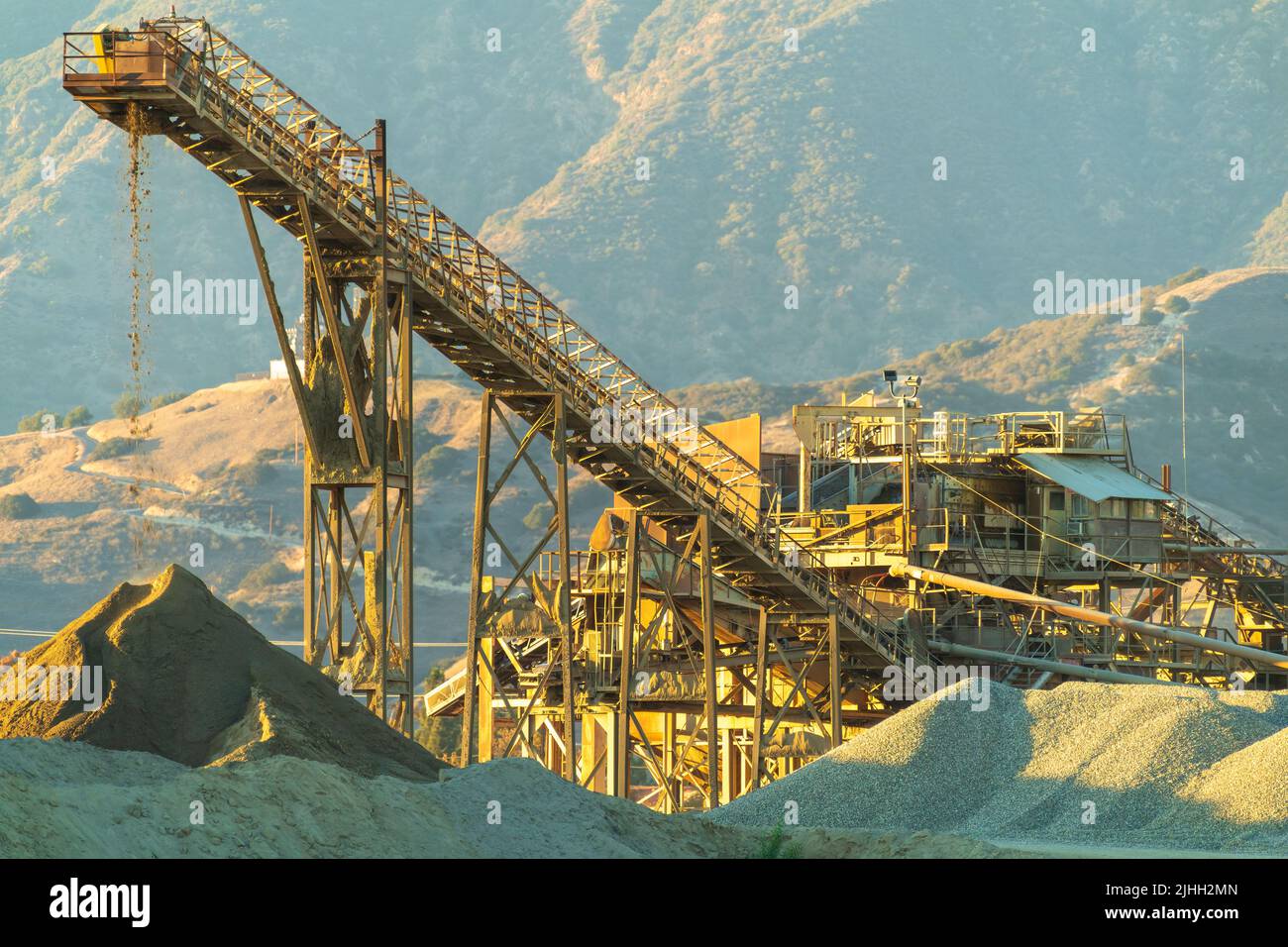 Il trasportatore a nastro trasporta la pietra frantumata dal macinacaffè al cumulo al tramonto. Foto Stock