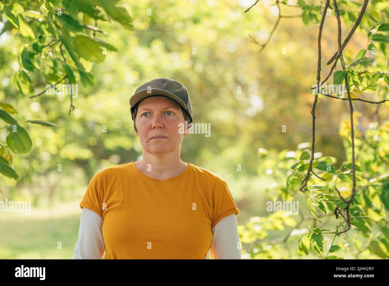 Ritratto di lavoratrice agricola femminile con t-shirt arancione e cappello di camionista in frutteto di noce, fuoco selettivo Foto Stock