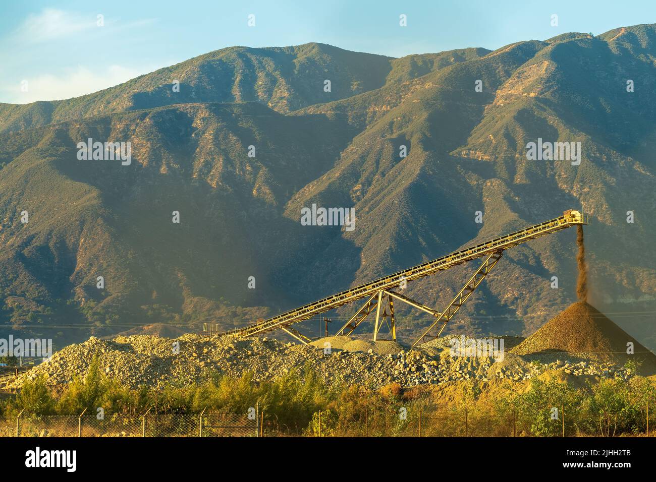 Il trasportatore a nastro trasporta la pietra frantumata dal macinacaffè al cumulo al tramonto. Foto Stock
