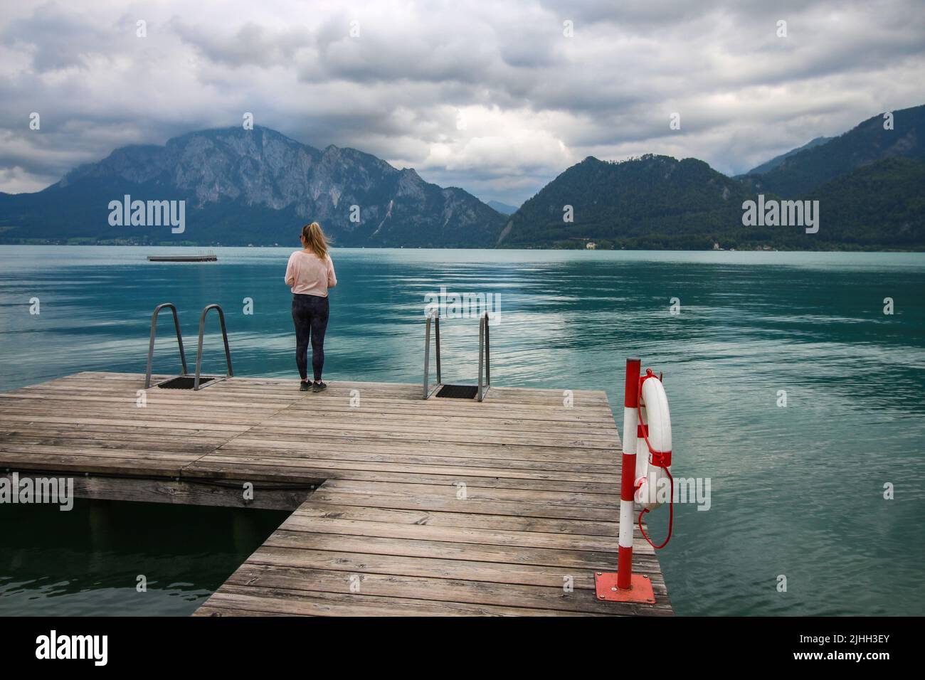 Attersee - famoso lago turchese austriaco. La vista sulla donna in piedi sul molo di legno guardando il lago e le belle montagne nuvolose nel Foto Stock