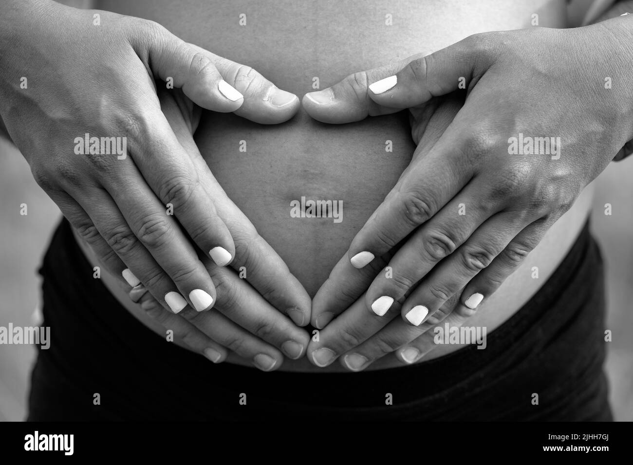 Immagine bianca e nera della coppia che tiene le loro mani sopra il ventre delle madri che si aspetta un bambino Foto Stock