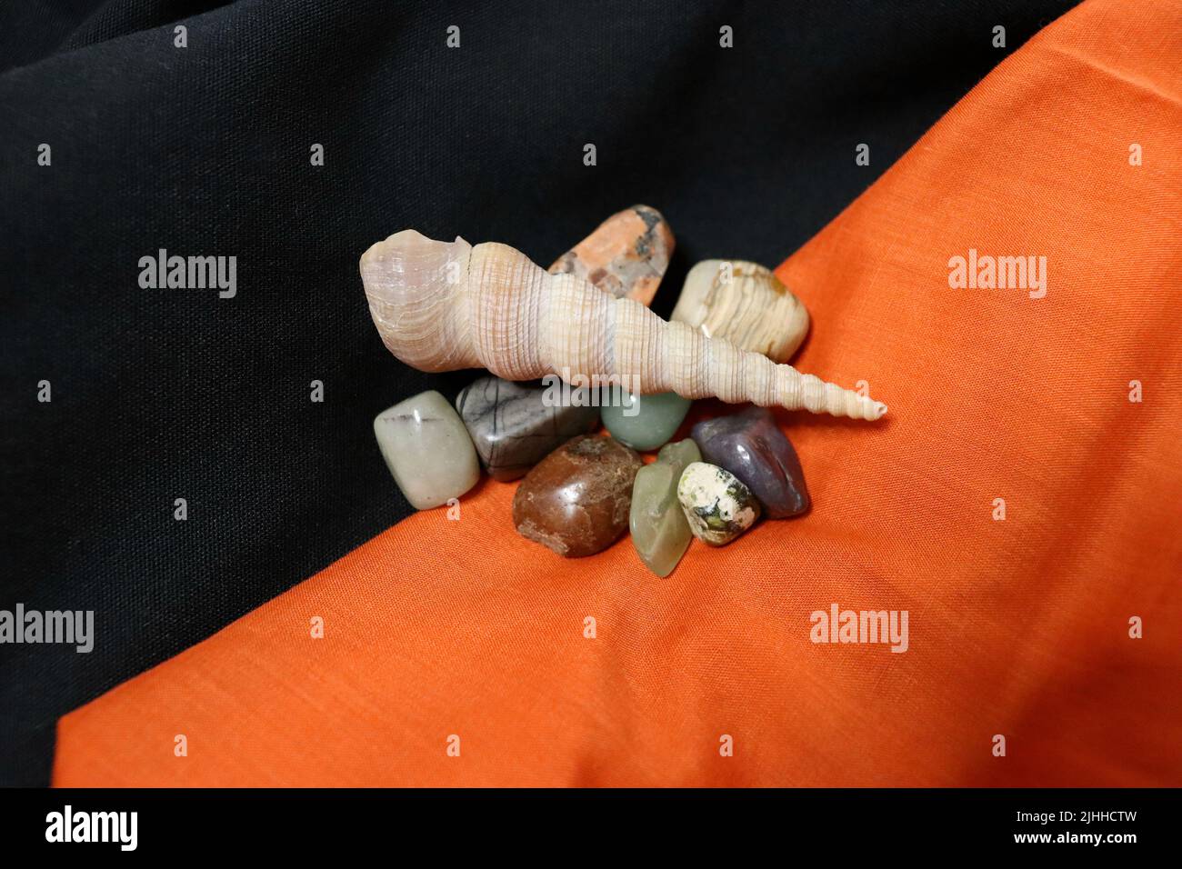 Un gruppo di pietre preziose lucidate sopra i tovaglioli neri e arancioni di tessuto con un guscio di coclea. Foto Stock
