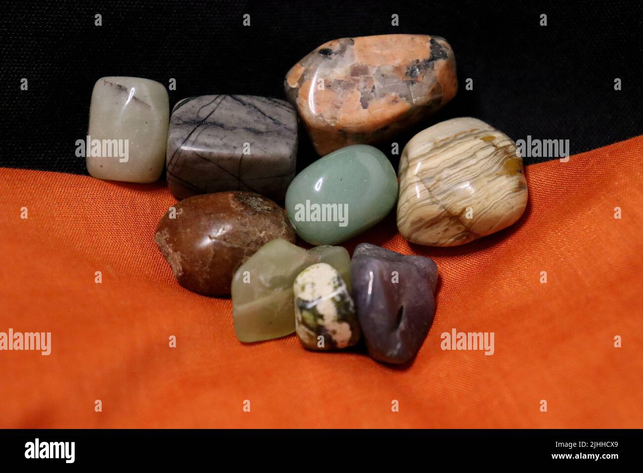 Un gruppo di pietre preziose lucidate sopra i tovaglioli neri e arancioni di tessuto con un guscio di coclea. Foto Stock