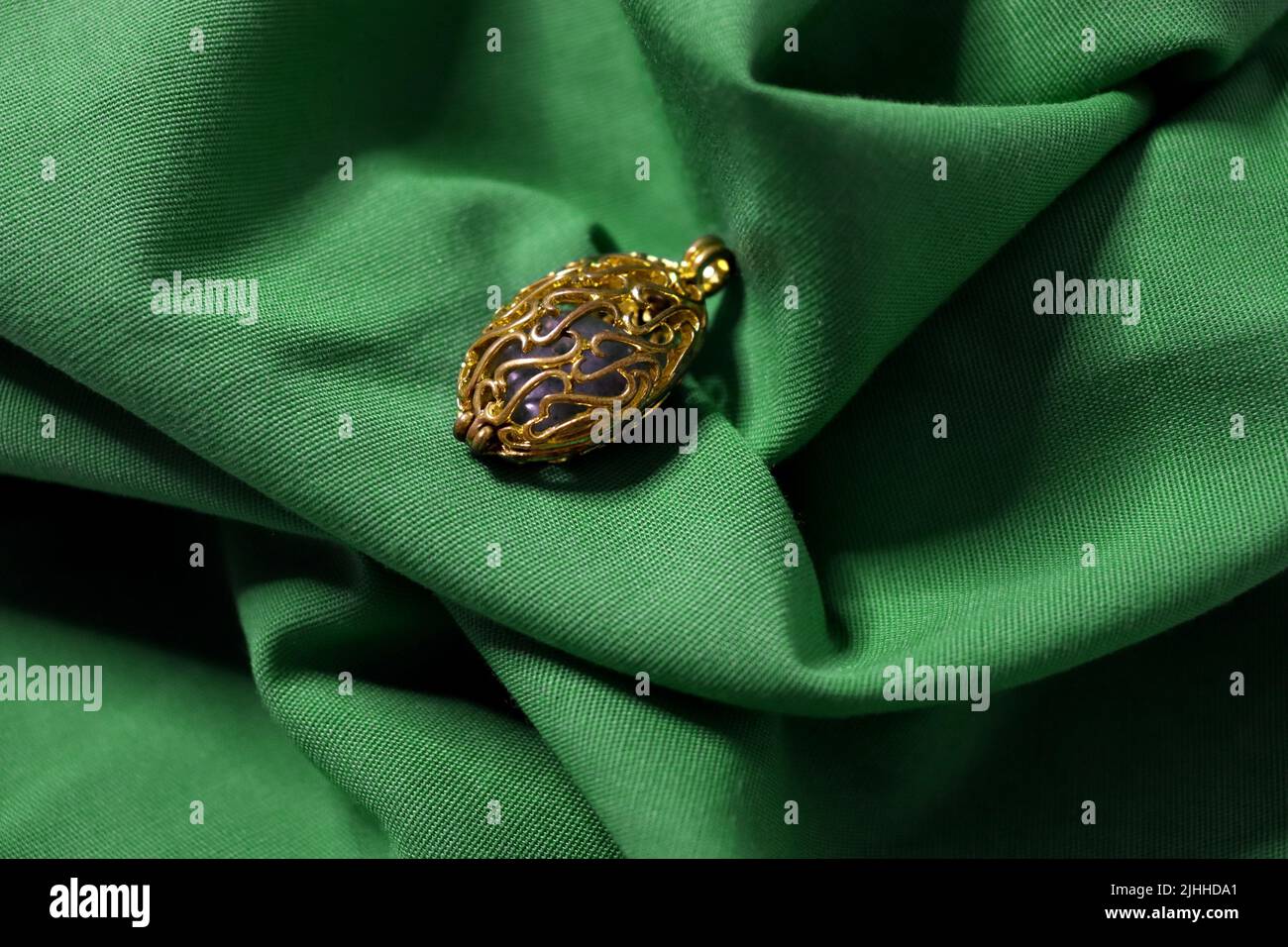 Un buco filigrana in oro cavo con un pezzo di pietra verde all'interno seduto su un grinzito di tessuto verde vibrante. Foto Stock