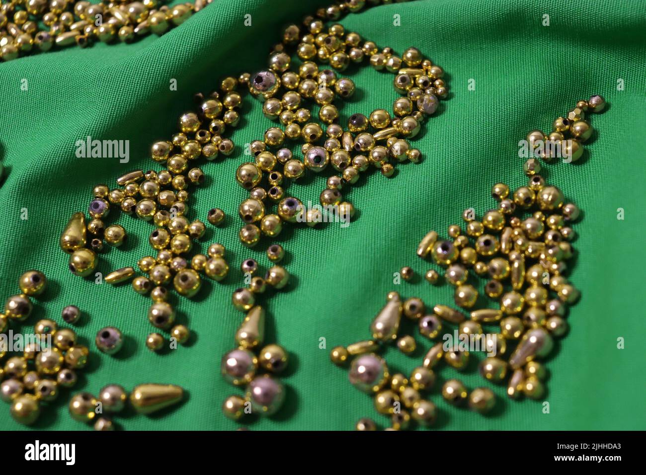 Una tonnellata di perle d'oro in varie forme si è rovesciata su un panno verde brillante leggermente stropicciato. Primo piano. Nessun filtro. Foto Stock