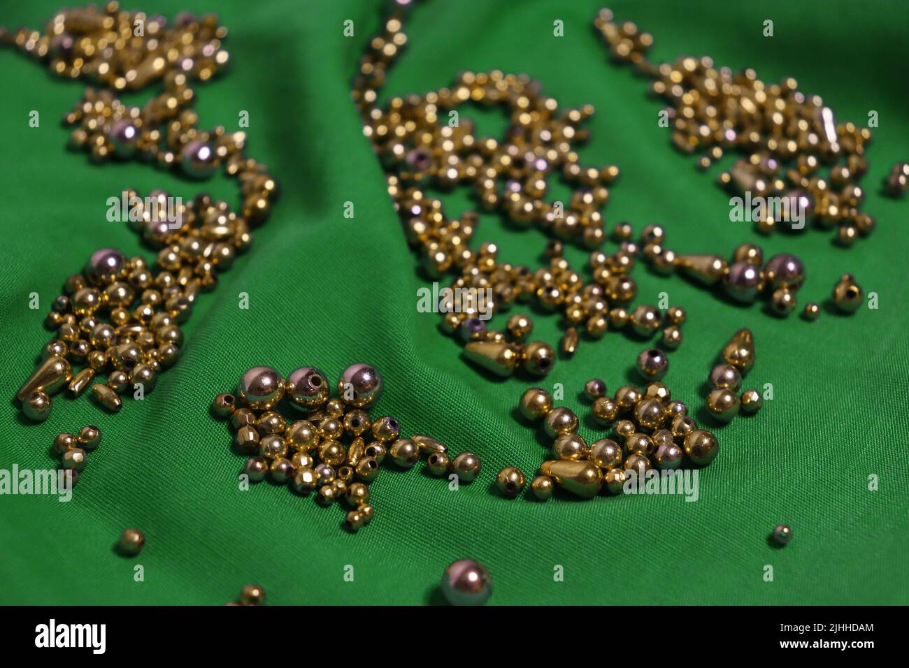 Una tonnellata di perle d'oro in varie forme si è rovesciata su un panno verde brillante leggermente stropicciato. Primo piano. Nessun filtro. Foto Stock