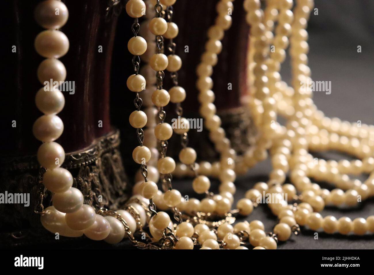 Un mucchio di varie collane di perle da vicino e su uno sfondo neutro con elementi aggiuntivi come un vaso, vecchio cappello, maschera, e canister rosso/oro di stoccaggio. Foto Stock