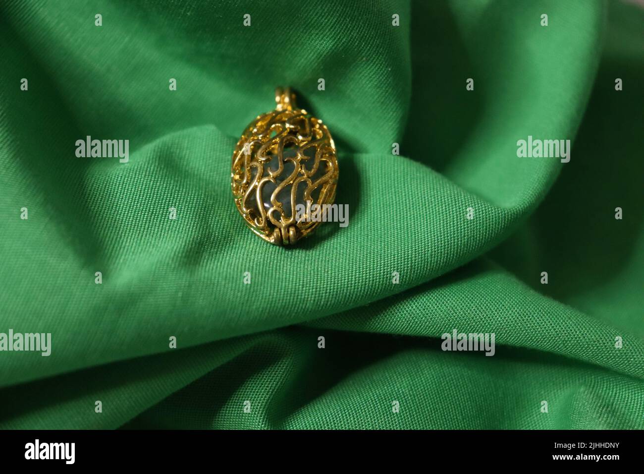 Un buco filigrana in oro cavo con un pezzo di pietra verde all'interno seduto su un grinzito di tessuto verde vibrante. Foto Stock