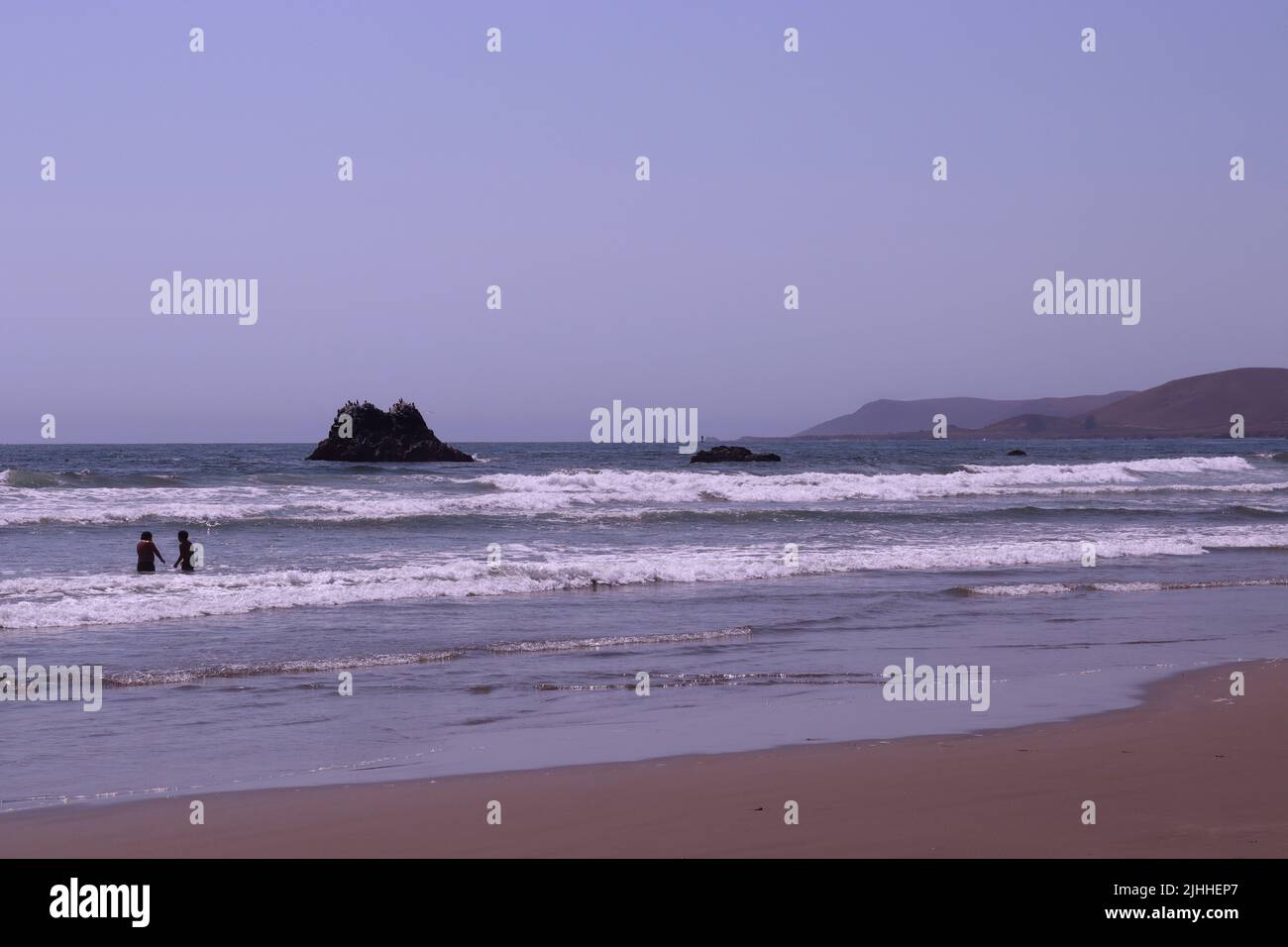 Un pomeriggio tranquillo e leggermente coperto su una spiaggia vicino Cayucos, CA con poche persone e dolci onde. Morro Bay si trova in lontananza con la sua roccia gigante. Foto Stock