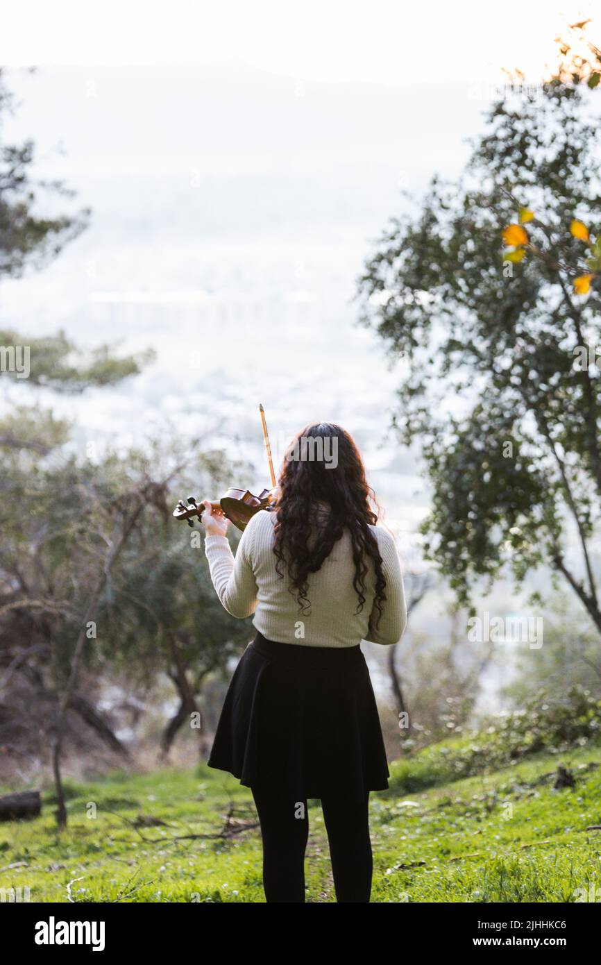 Donna bruna vista dalla parte posteriore giocando il violino fuori nella montagna. Verticale Foto Stock