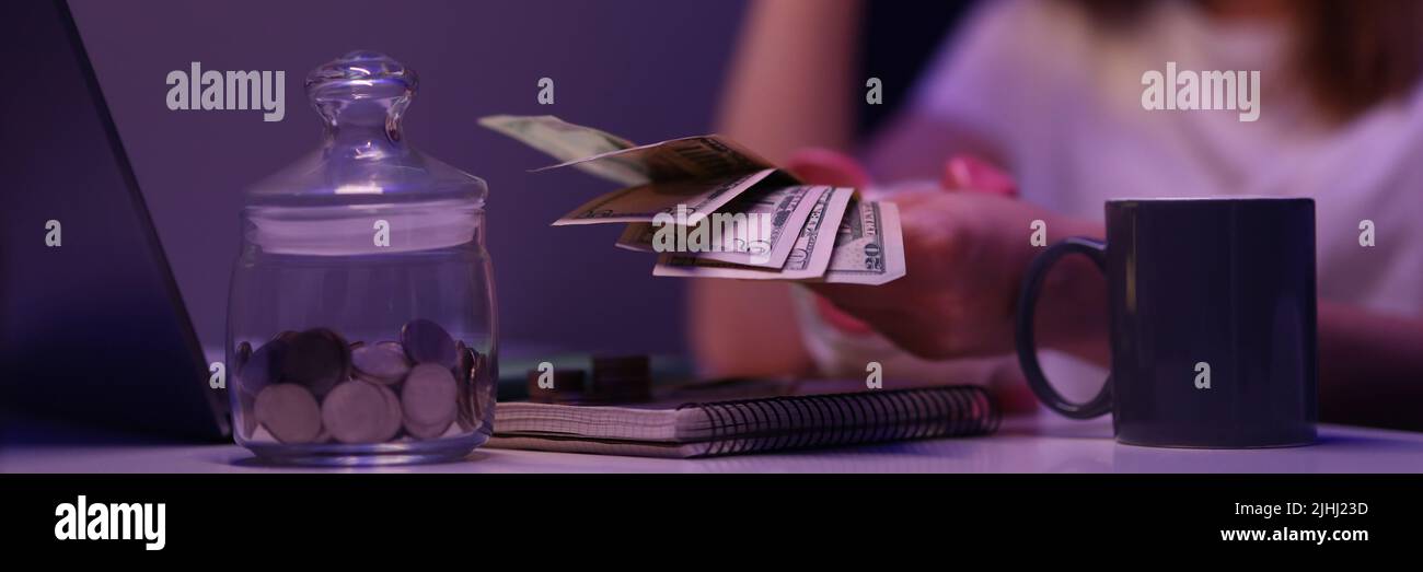 Ragazza rotta contando denaro contante, contenitore di vetro con monete sulla scrivania Foto Stock