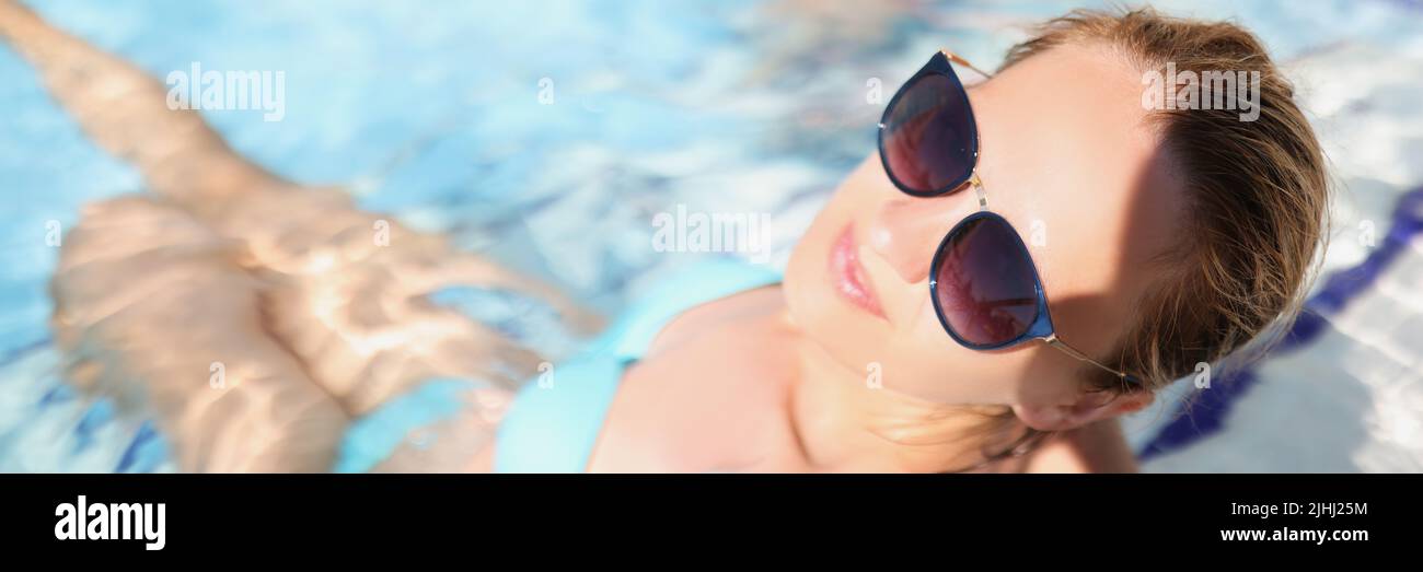 Felice giovane femmina seduta in piscina con occhiali alla moda Foto Stock