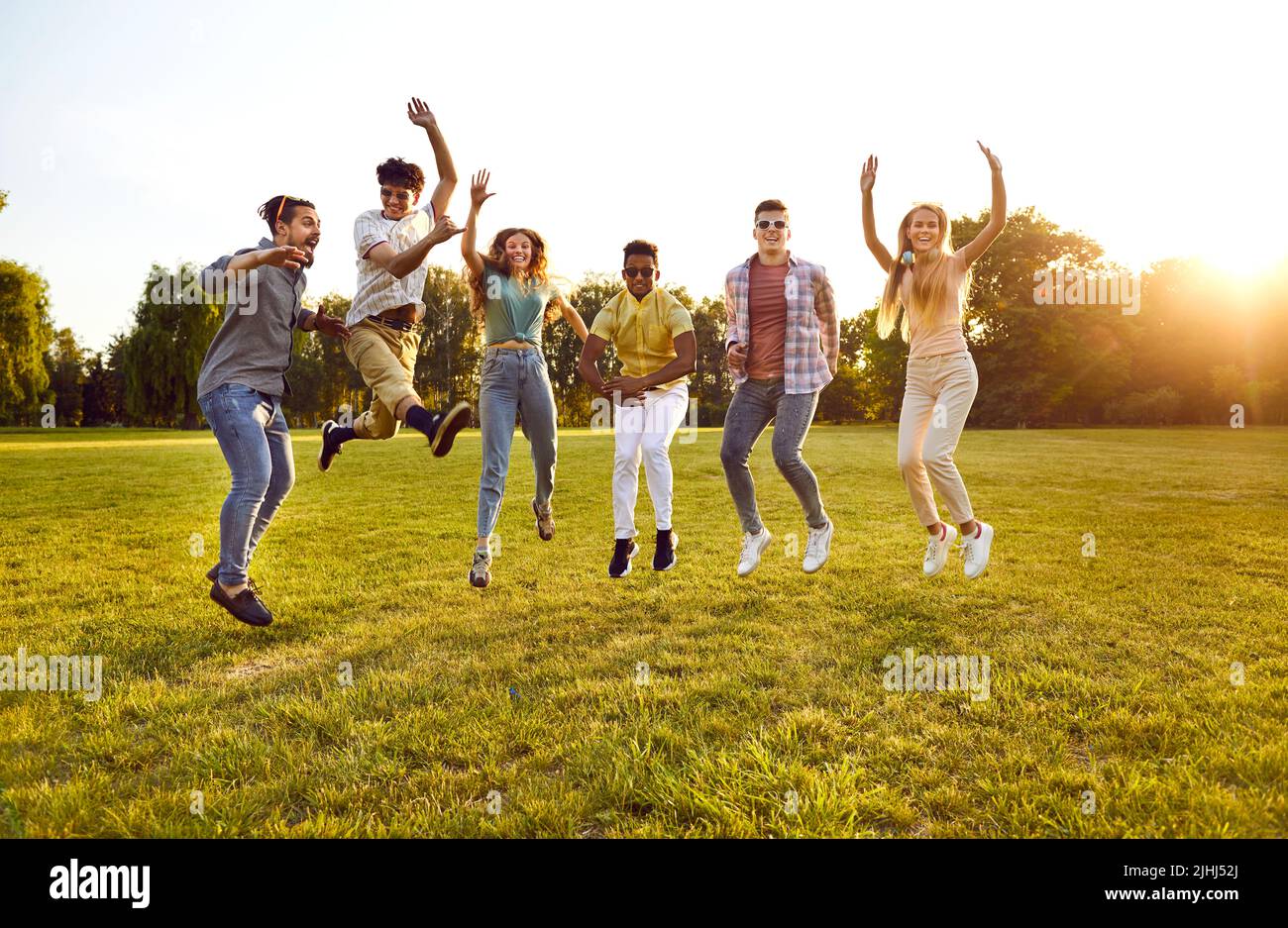 Gruppo multircial di amici felici ed eccitati che saltano sul prato verde del parco tutti insieme Foto Stock