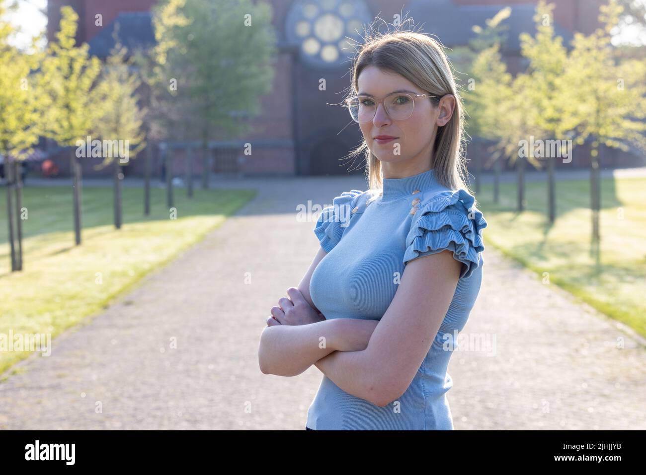 Affascinante modello giovane donna con occhiali e blusa blu in estate giorno di sole all'aperto e guardando lontano. Sottile caucasica bella ragazza a piedi nel parco. Foto di alta qualità Foto Stock