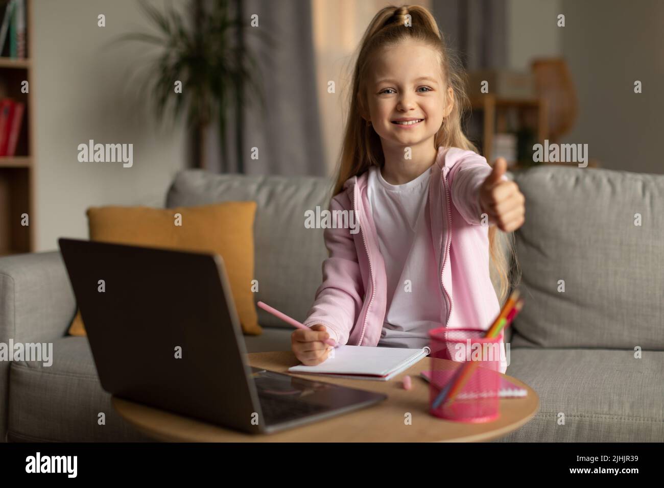 Studentessa al notebook gesturando i thumbs fino alla macchina fotografica a casa Foto Stock