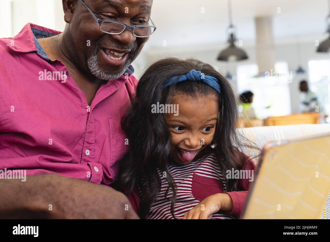 Felice nonno multirazziale con la nipote fare il viso guardando video su tablet digitale Foto Stock