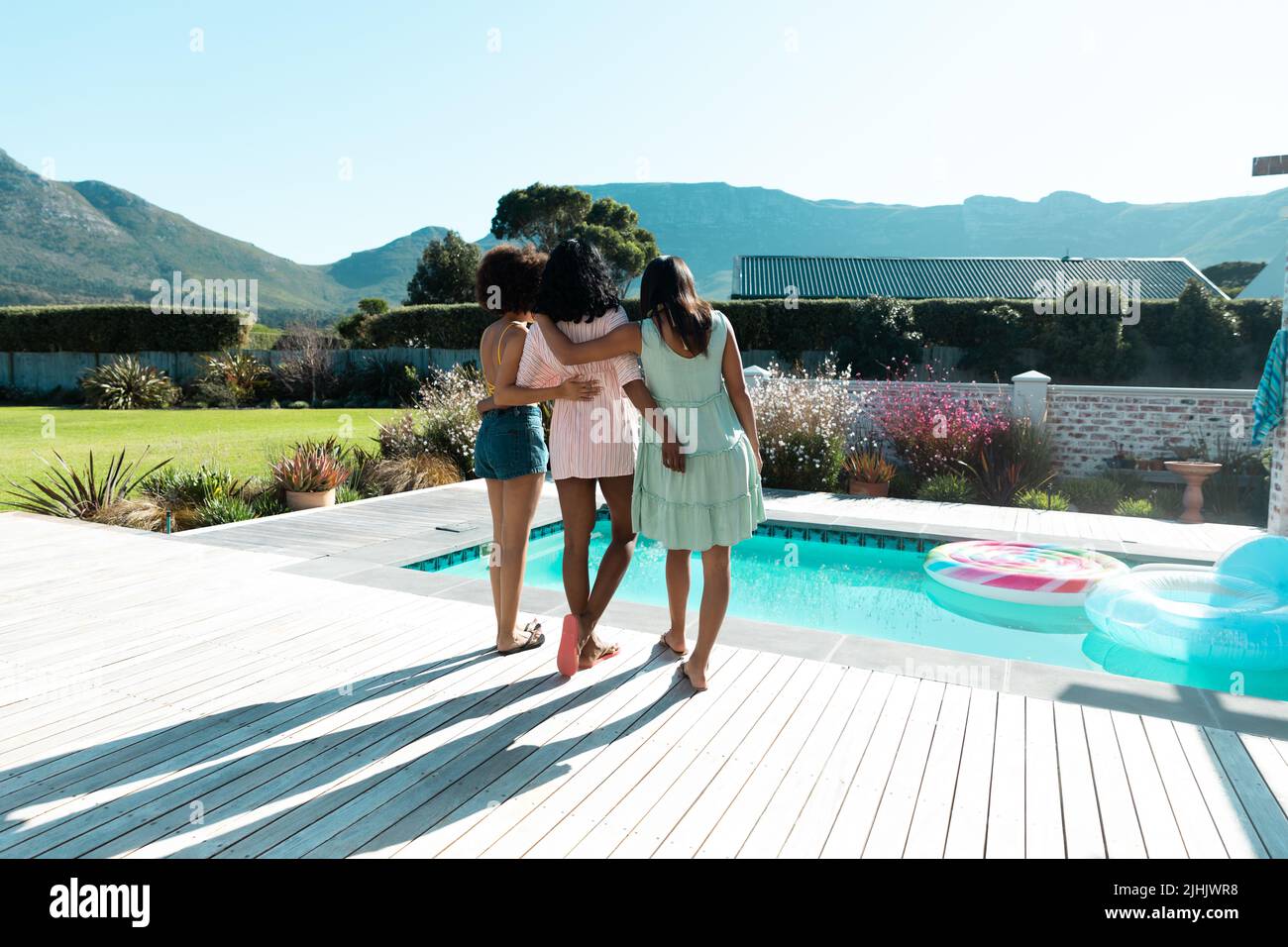 Giovani amiche biraciali con le braccia intorno appese a bordo piscina durante l'estate, spazio copia Foto Stock