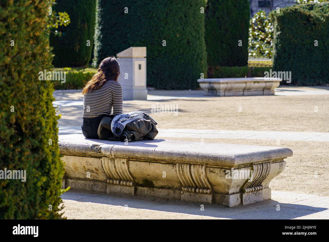 Donna seduta sulla schiena su una panchina in un parco pubblico, godendo di una giornata di sole. Madrid. Foto Stock