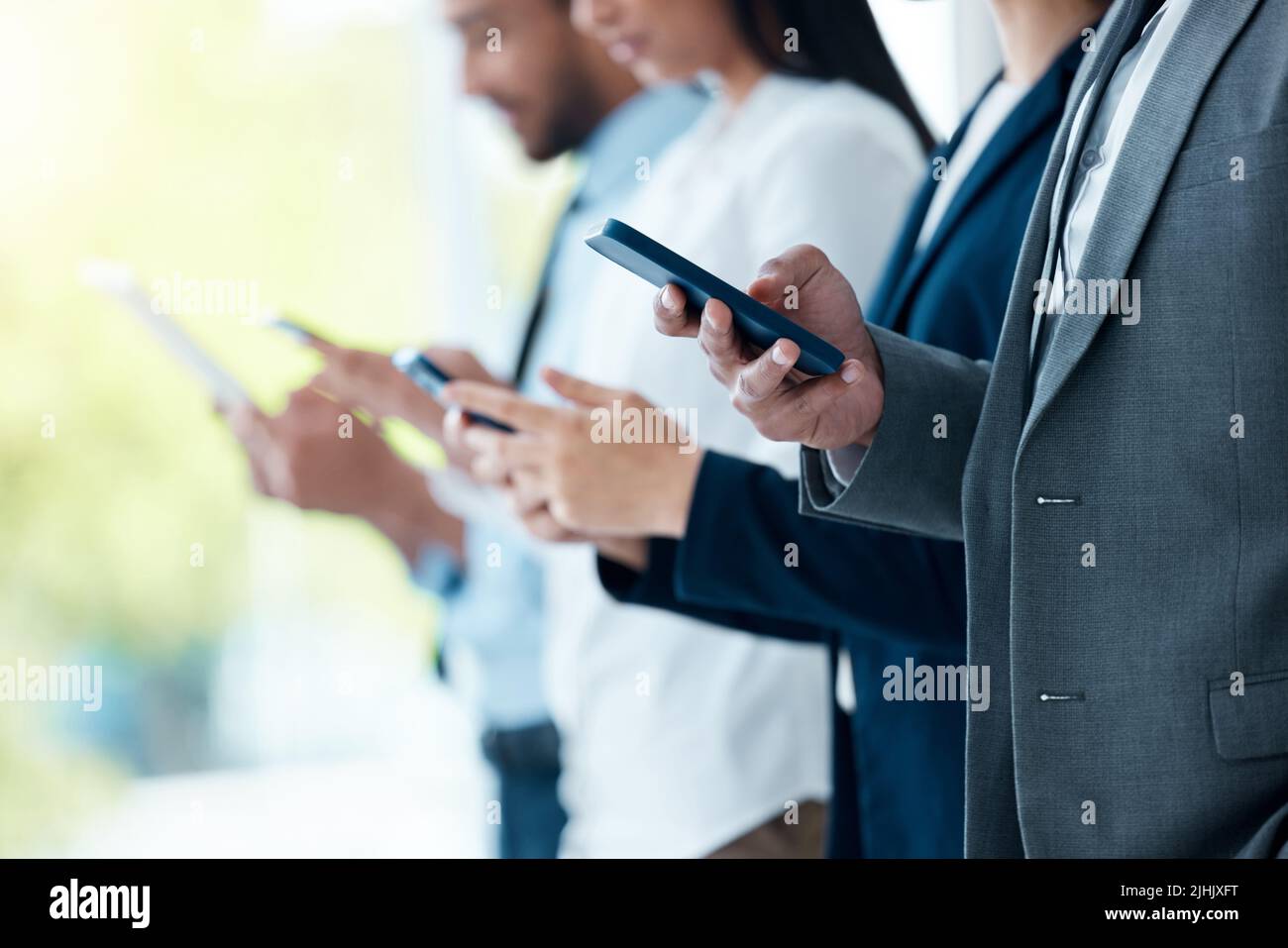 Nessuno di noi è intelligente come tutti noi. Un gruppo di uomini d'affari inriconoscibili che utilizzano i loro dispositivi in un ufficio moderno. Foto Stock