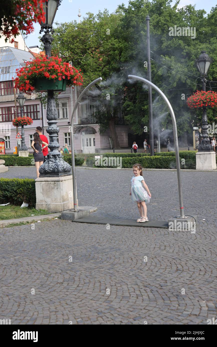 Le ragazze piccole carine amano il raffreddamento dai nebulizzatori pubblici su una piazza della città; raffreddamento della nebbia dell'acqua, spruzzatori d'acqua Foto Stock