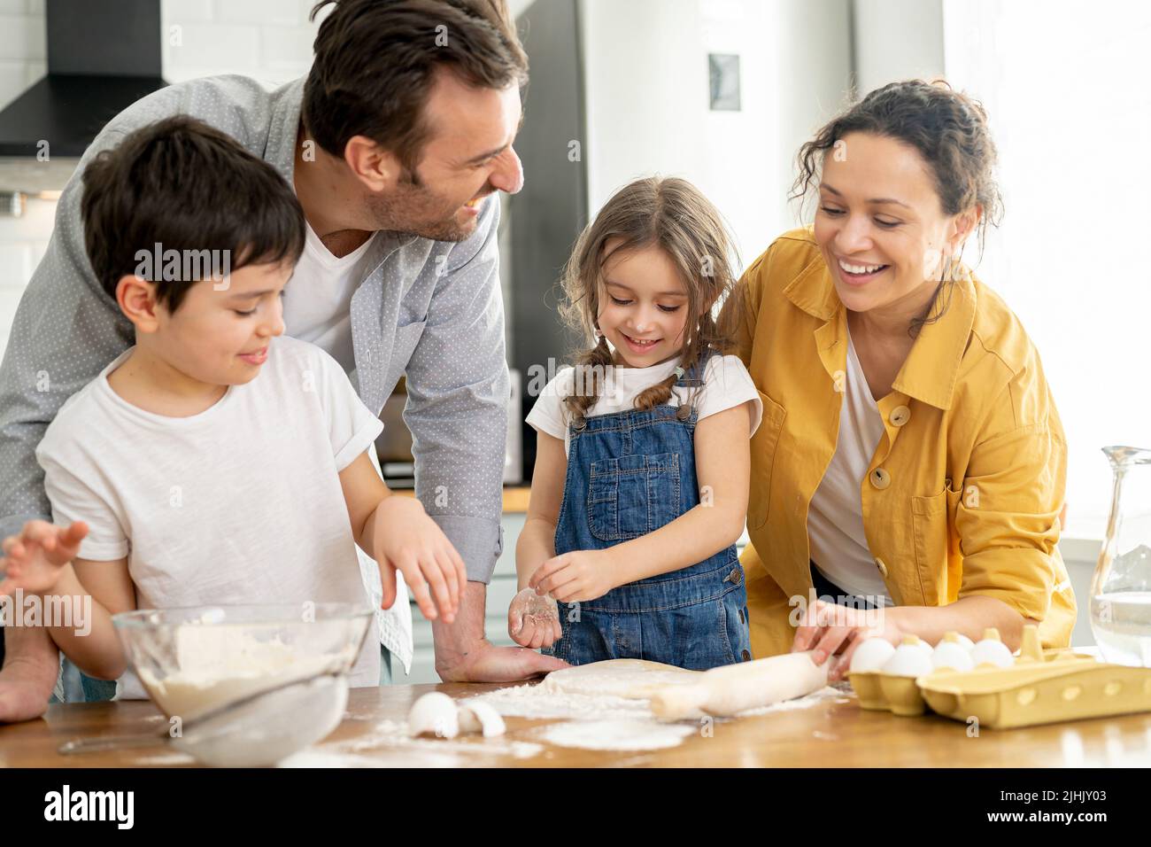 Famiglia felice di quattro cucinare in cucina insieme, genitori e due bambini che fanno pasta insieme, preparare torta o biscotti, divertirsi il fine settimana Foto Stock