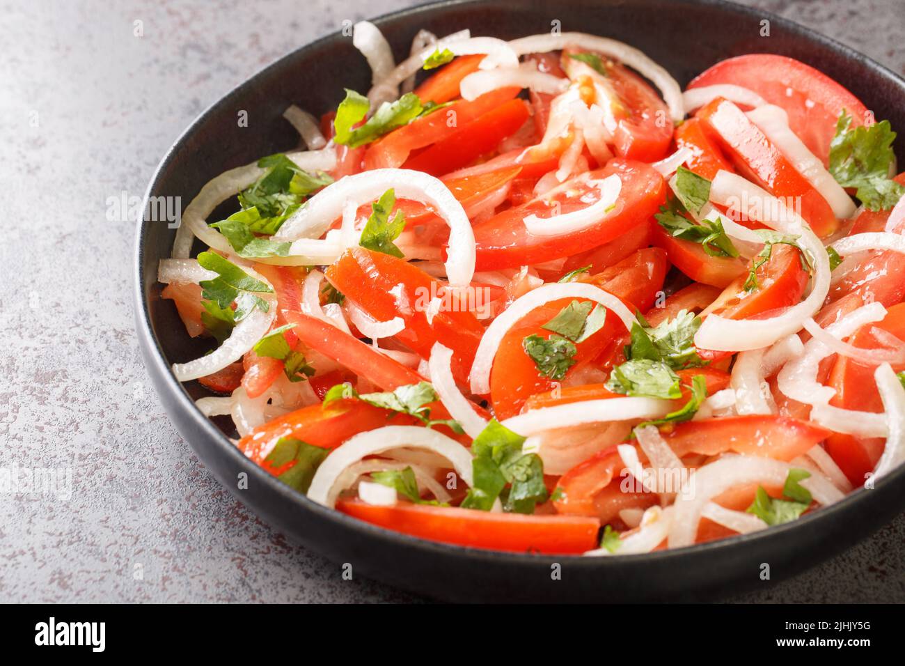Concetto sano antipasto pomodori freschi con cipolla e spezie primo piano nel piatto sul tavolo. Orizzontale Foto Stock