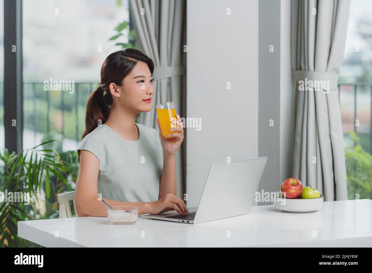 bella giovane donna che lavora con il computer portatile durante la colazione con cereali e latte e bere succo d'arancia Foto Stock