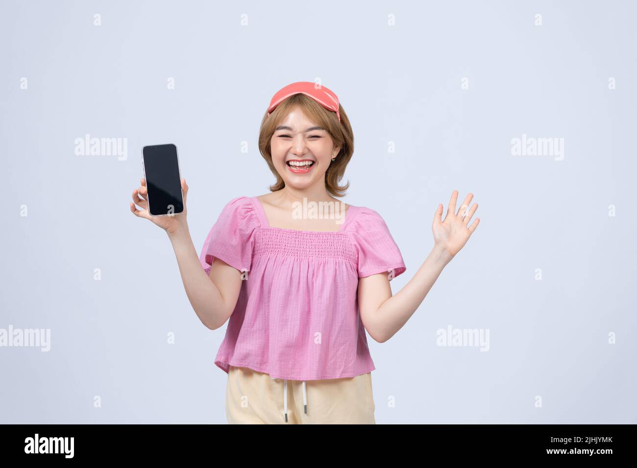 happy ragazza guardare la fotocamera tenere telefono cellulare in mani indossare rosa maschera di sonno ottenere buone notizie Foto Stock