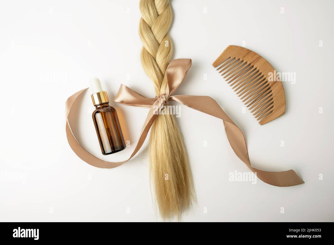 Un olio naturale o siero per il trattamento dei capelli e una treccia di capelli biondi con arco giacente su sfondo bianco Foto Stock