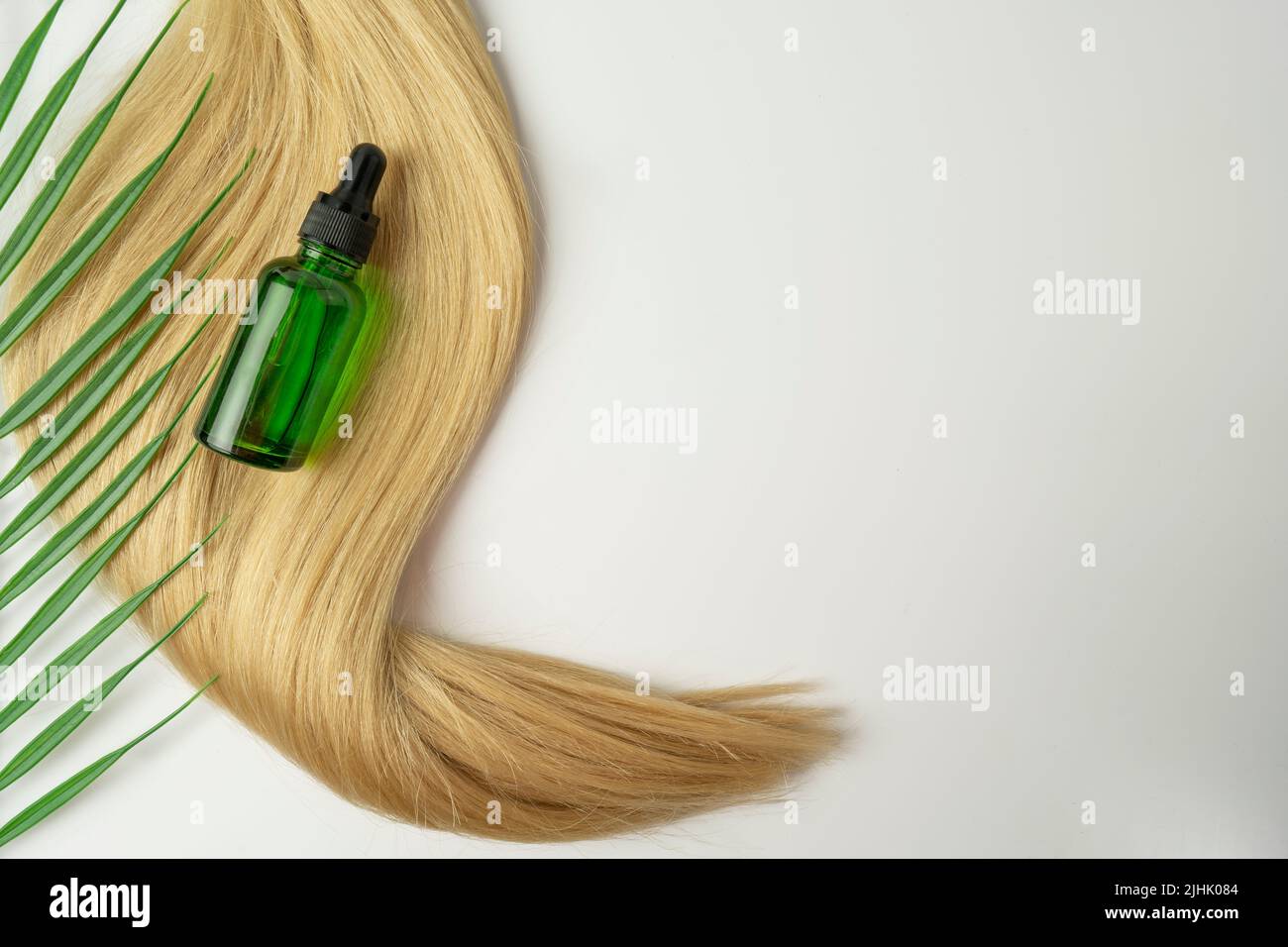 Un olio naturale o siero per la cura dei capelli che giace su una tela di capelli biondi Foto Stock