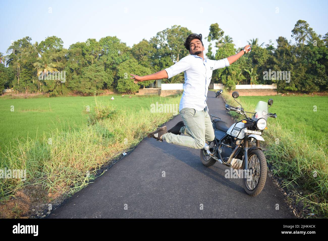 Un uomo in posa per una foto con moto vicino al campo di risaie Foto Stock