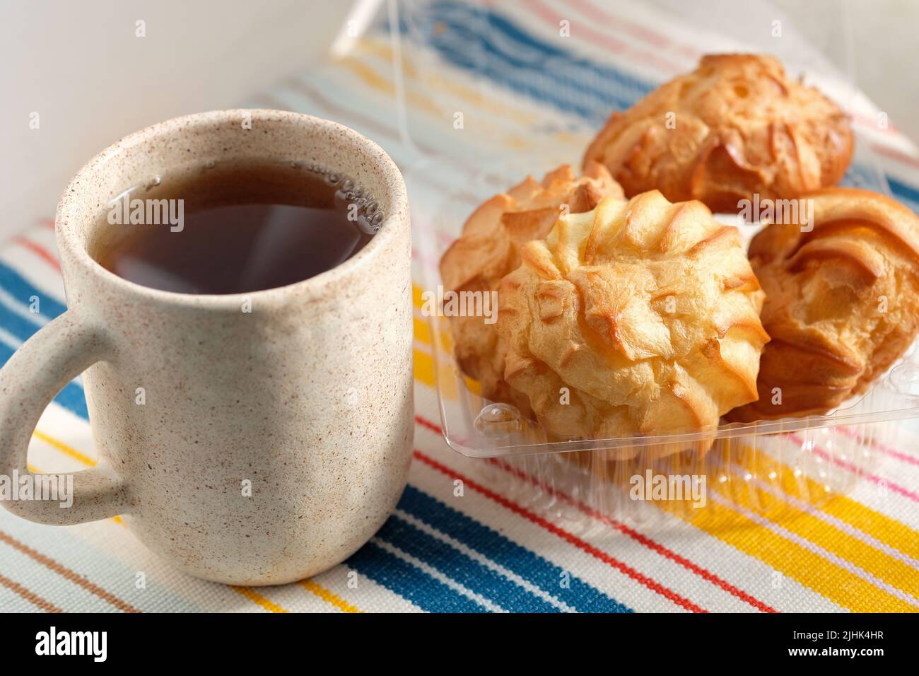 Panna puffs torte o profiterolo riempito con panna montata in scatola di plastica. eclairs e una tazza di tè in ceramica. Dessert tradizionale francese gustoso. Foto Stock
