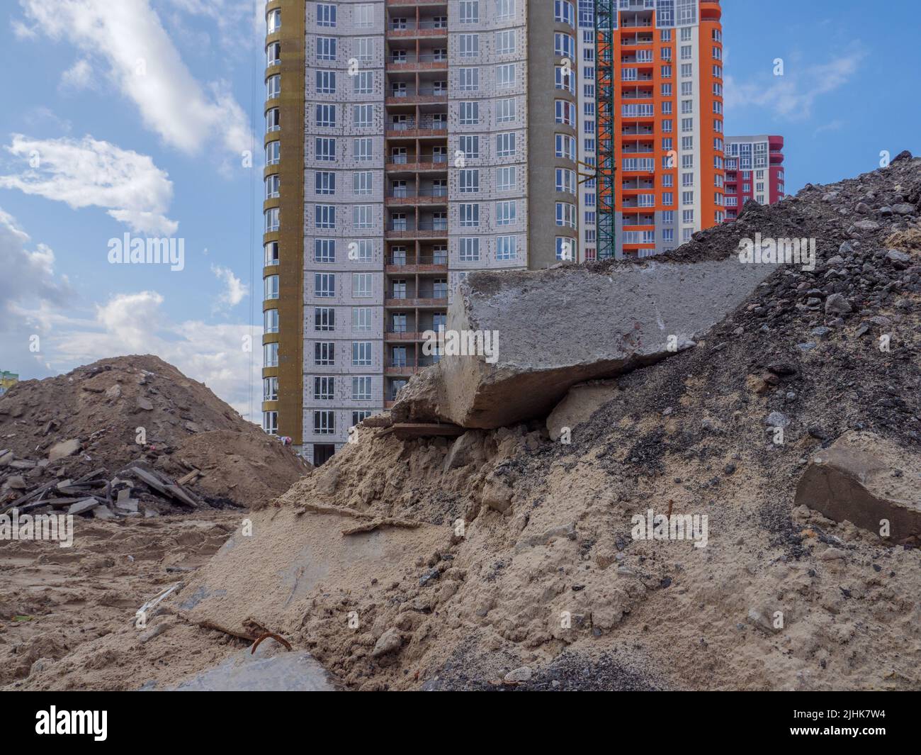 Un cantiere con mucchi di sabbia, enormi blocchi di cemento e rifiuti da costruzione in primo piano e nuovi alti edifici sullo sfondo a Kyiv. Foto Stock