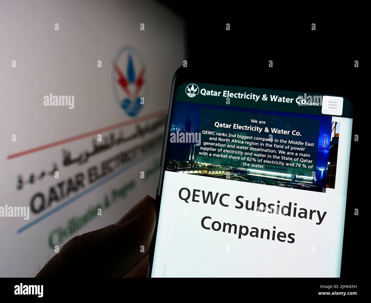 Persona che detiene il cellulare con il sito web della società Qatar Elettricità acqua Company (QEWC) sullo schermo con il logo. Concentrarsi sul centro del display del telefono. Foto Stock