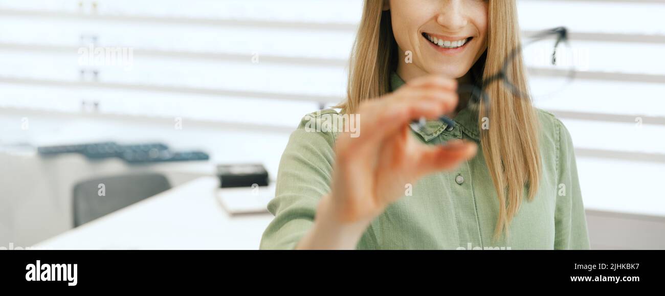 donna sorridente che sceglie nuovi occhiali in negozio di occhiali ottici. banner con spazio copia Foto Stock