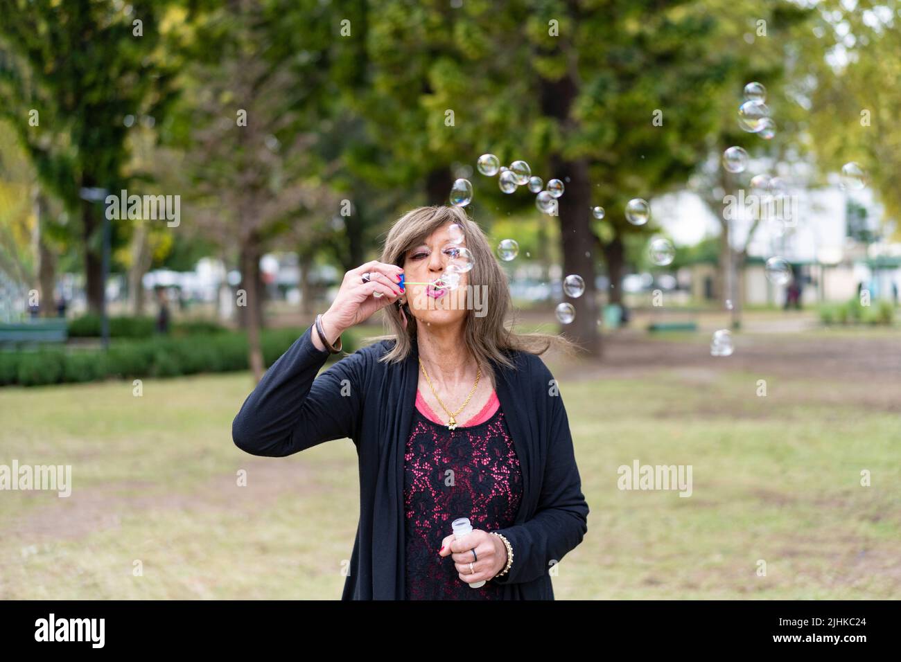 Donna trans matura che soffia bolle in un parco Foto Stock