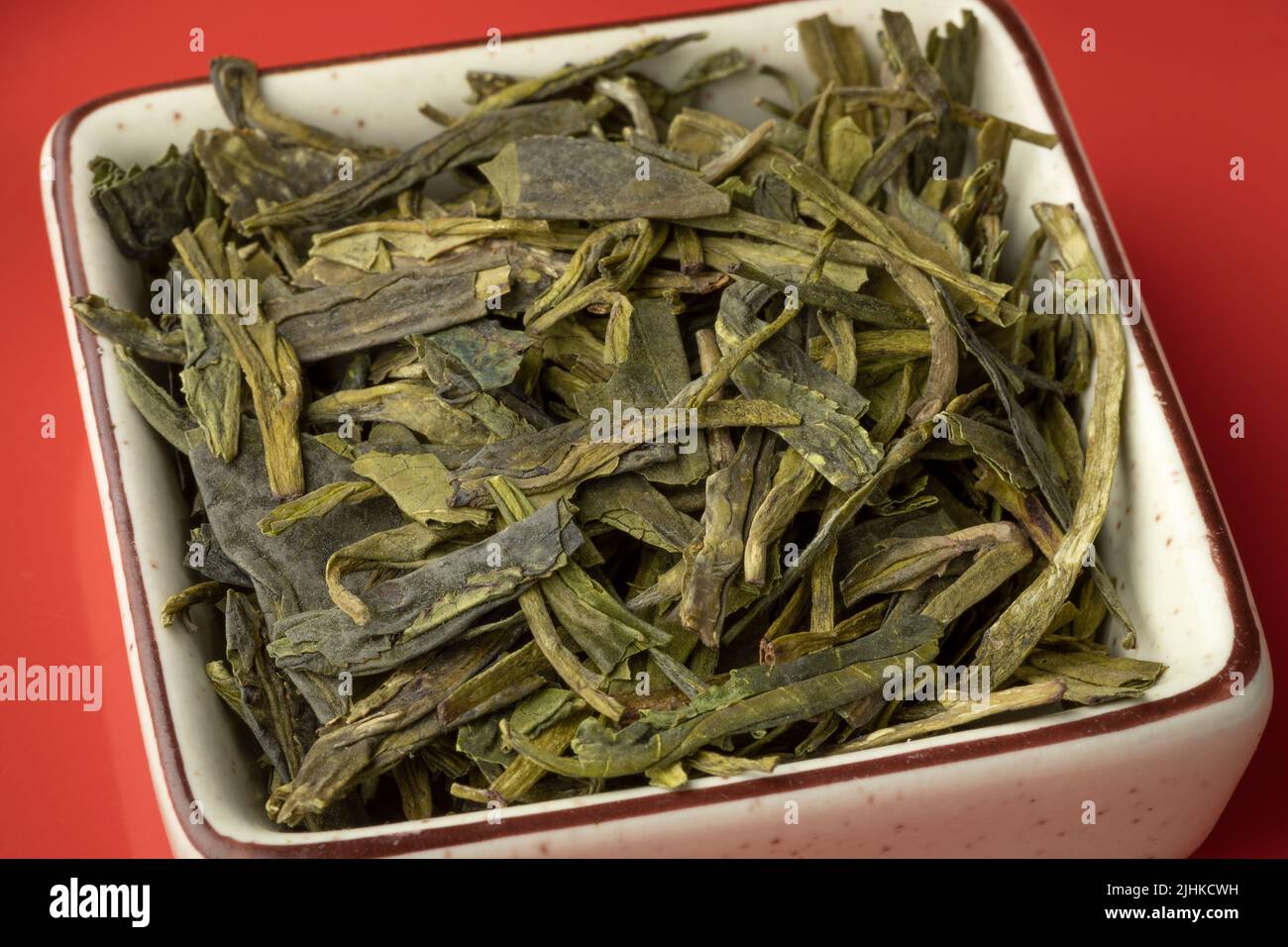 Ciotola con le foglie di tè di ChineseLung Ching secche da vicino su sfondo rosso Foto Stock