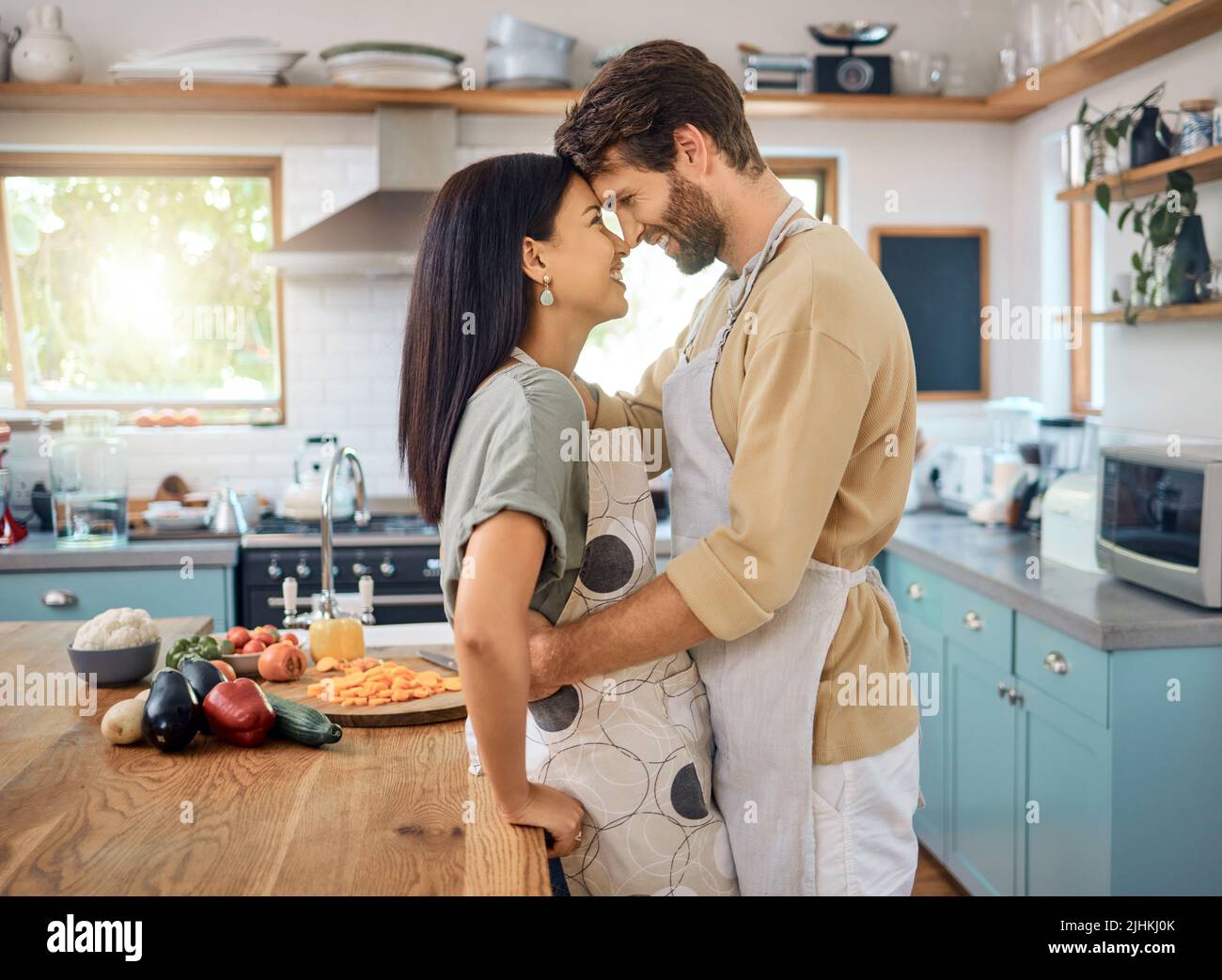 Felice coppia interrazziale toccare fronte mentre condividere romantico momento intimo a casa, indossando grembiuli e cucinare insieme. Giovane caucasico Foto Stock
