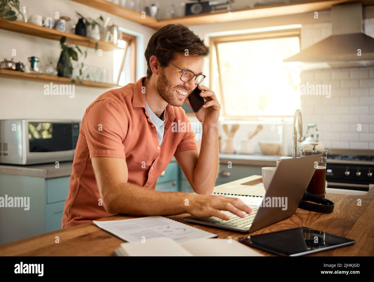 Giovane soddisfare caucasico uomo d'affari che indossa gli occhiali su una chiamata usando un telefono mentre lavora su un laptop nel paese da solo. Felice uomo d'affari maschile sorridente Foto Stock