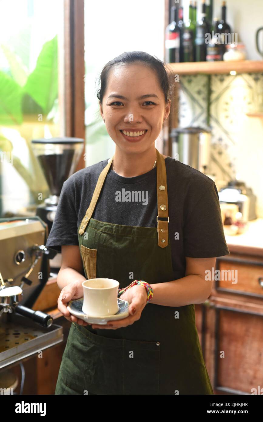 Donna asiatica cameriera che tiene una tazza di caffè fresco fatto Foto Stock