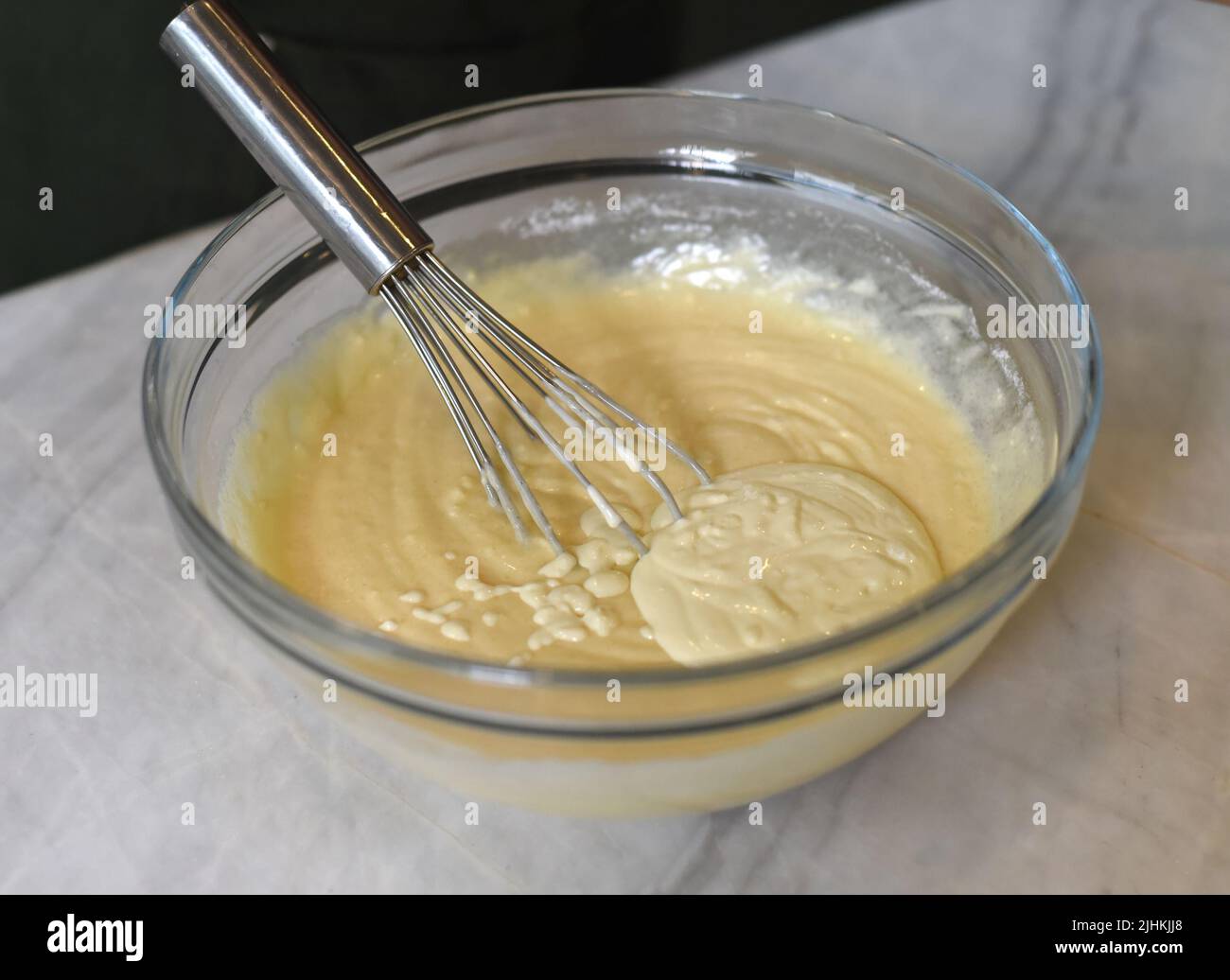 Frusta per le uova in un recipiente di vetro per mescolare l'impasto Foto Stock