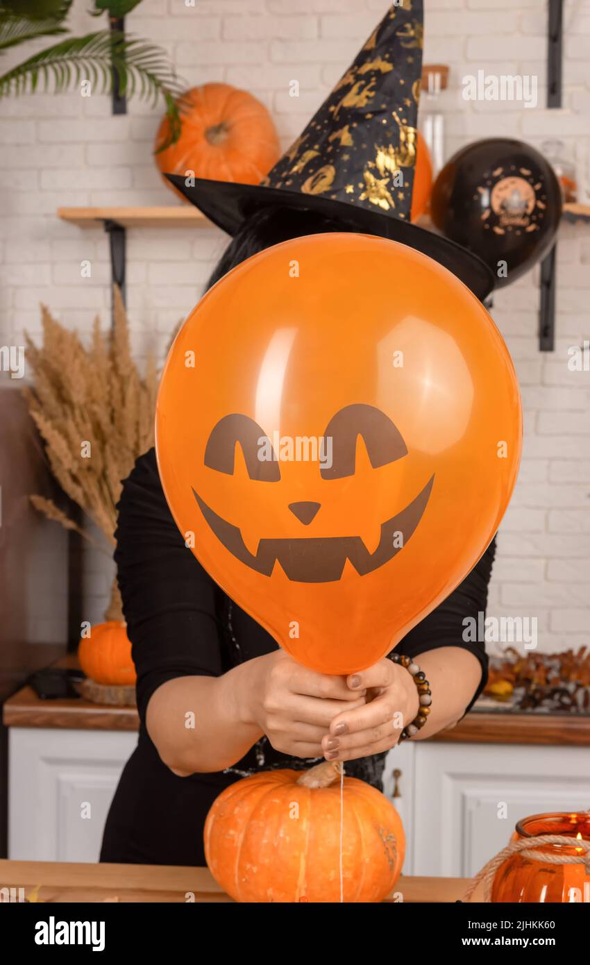 Una donna irriconoscibile che tiene un volto spaventoso di Halloween davanti al suo volto, un palloncino arancione luminoso. Una donna in un cappello a punta di carnevale nasconde il suo volto Foto Stock