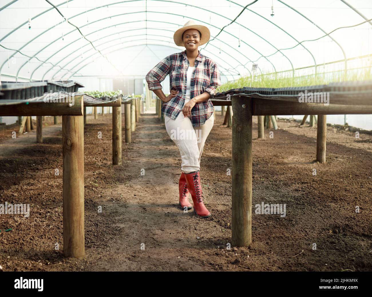 Corpo pieno di giovane agricoltore in un giardino. Ritratto di un agricoltore orgoglioso nella sua serra. Felice contadino afroamericano. Giovane agricoltore in piedi in lei Foto Stock